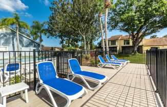 a patio with blue lounge chairs and a pool in the background