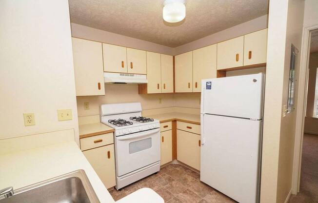 A two bedroom kitchen with a white refrigerator, stove, and sink at Foxwood and The Hermitage, Portage, MI
