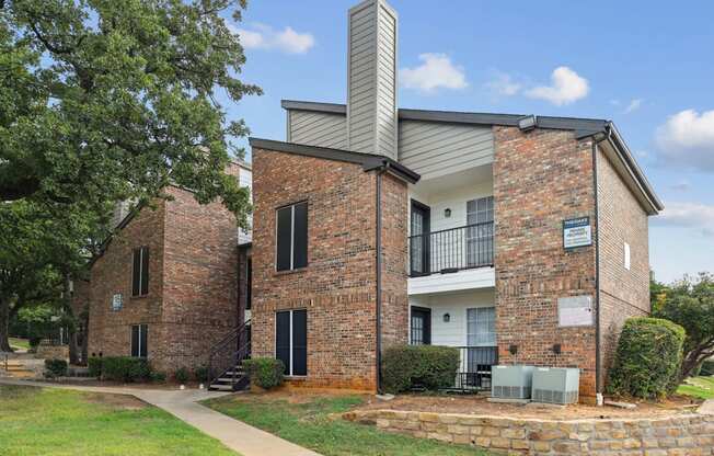 A two-story, brick apartment building with balconies and patios at The Oaks of Denton Apartments in Denton, TX