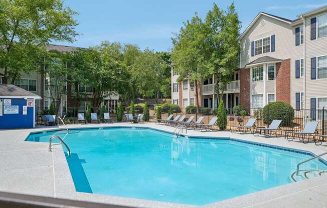A swimming pool surrounded by lounge chairs and trees in front of apartment buildings.