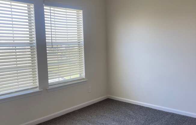 an empty room with two windows and a carpeted floor