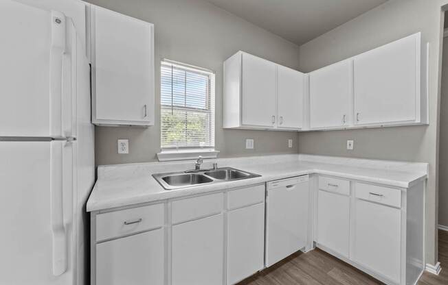 A white kitchen with a refrigerator, sink, and cabinets.