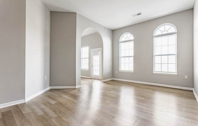 A room with wooden flooring and two windows.
