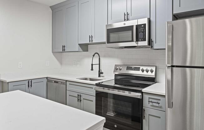 A modern kitchen featuring light blue cabinets, stainless steel appliances, including a microwave and oven, a silver refrigerator, and a white countertop. The design emphasizes a clean, contemporary aesthetic with a minimalist style and a bright atmosphere.