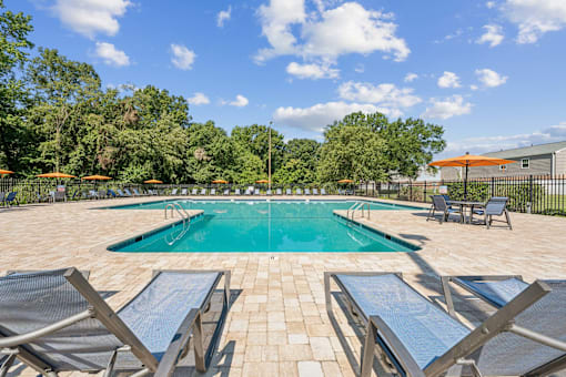 A pool surrounded by lounge chairs and umbrellas at Staples Mill Townhomes Apartments, Richmond, VA, 23228