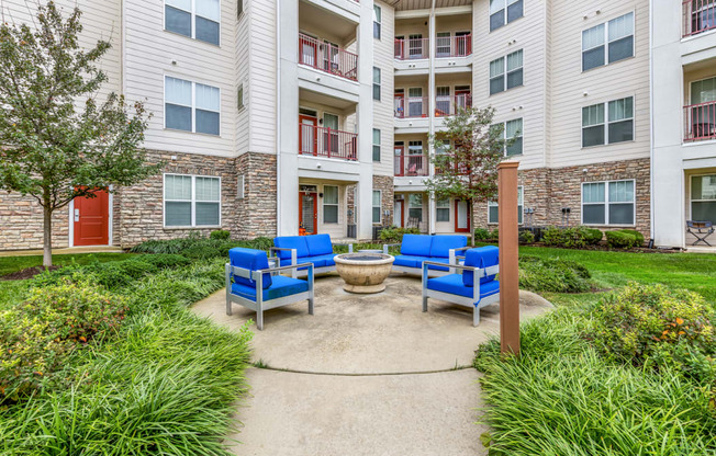 an outdoor patio with blue chairs and a fire pit in front of an apartment building