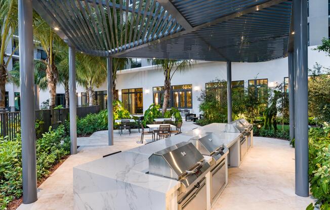 Outdoor kitchen design framed by a slatted canopy, marble prep surfaces, and layered tropical landscaping for effortless open-air gatherings in Miami.