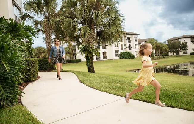 Little girl running on sidewalk with woman behind her at Lake Nona Water Mark in Orlando, FL