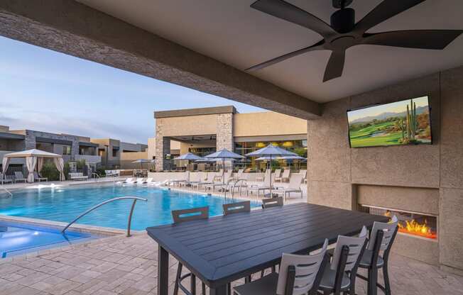 a patio with a table and chairs and a pool in the background