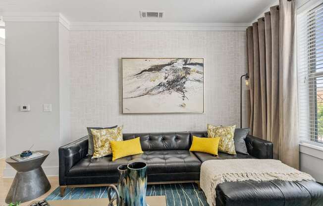 A living room with a black leather couch and a large abstract painting above it.