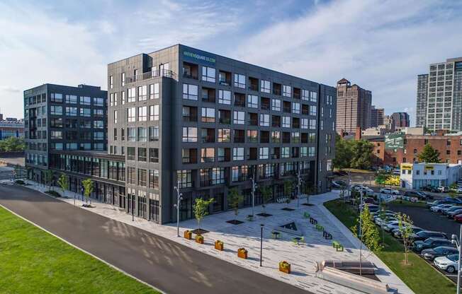 A modern multi-story building with a glass facade is surrounded by a parking lot and other buildings.