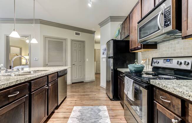 Kitchen with brown cabinetry, granite countertops, and stainless steel appliances at Avenues at Craig Ranch apartments for rent