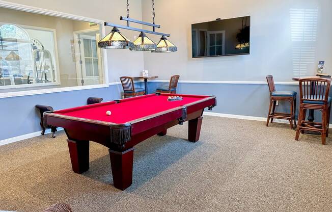 a red pool table in a game room with chairs and a tv