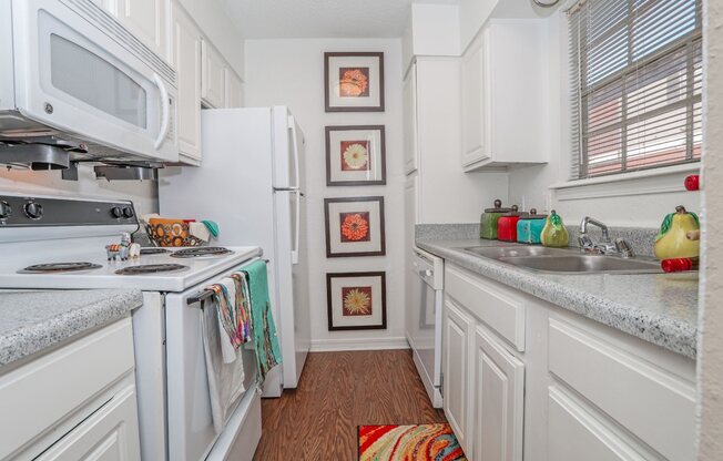 Furnished model apartment kitchen with wooden floors, white appliances, and four framed pictures on the wall at Magnolia apartments in Shreveport, LA