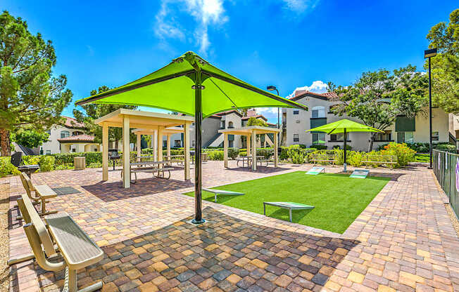 A sunny day at the park with a green umbrella and benches.