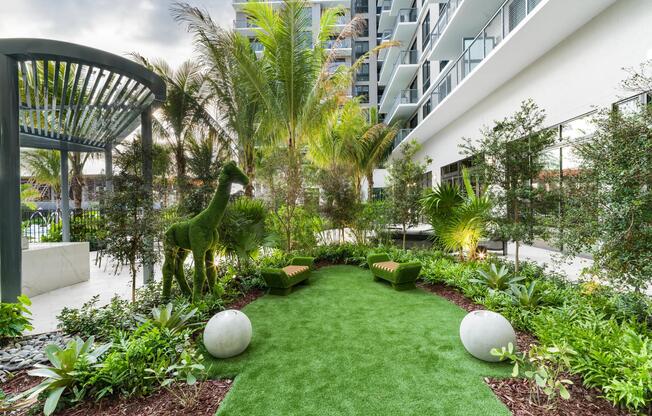A sculptural garden courtyard at Modera Aventura, where tropical landscaping, playful art, and shaded seating create a distinctive outdoor retreat.
