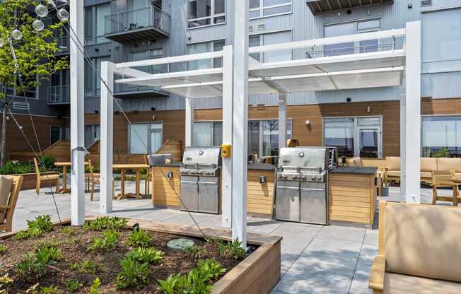 A patio with a grill and chairs is surrounded by a building.