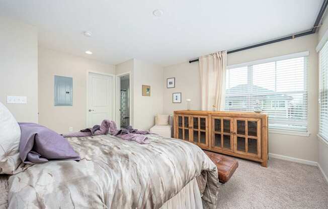 A bedroom with a bed, a window with blinds, and a wooden cabinet.