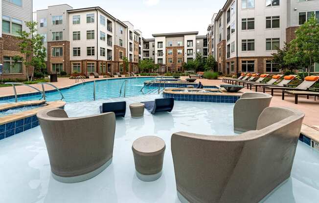 a large swimming pool with chairs around it in front of an apartment building
