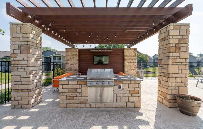 an outdoor kitchen with a grill and a tv under a pergola