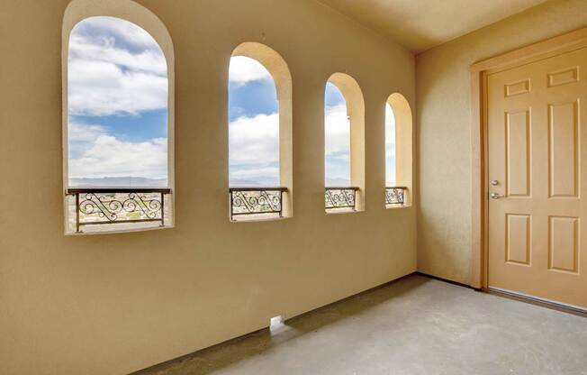 A room with a brown door and three windows with a view of the sky.