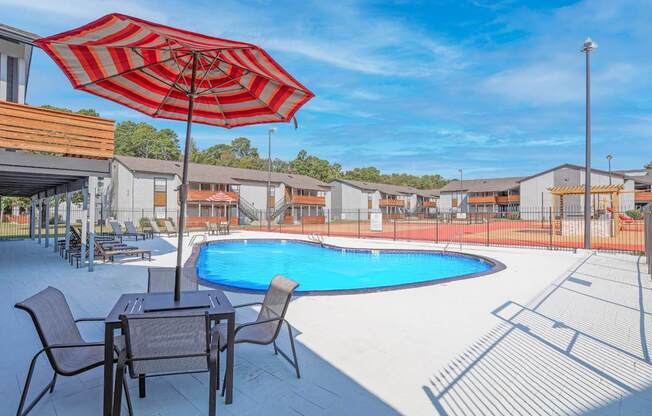 A red and white striped umbrella is over a table with chairs by a pool at The Marq apartments in Shreveport, LA