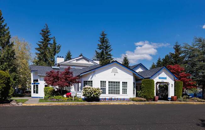 A white house with a blue roof and a red tree in front.