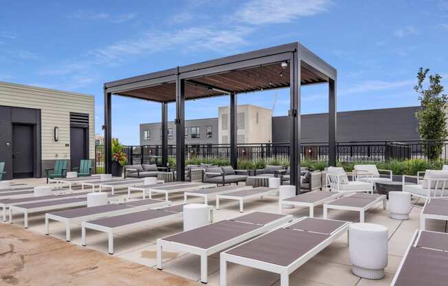 a group of white lounge chairs and umbrellas on a patio with buildings in the background