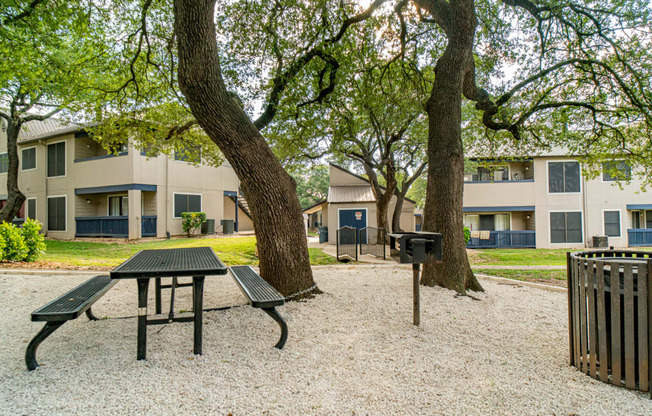 a park with a picnic table and a trash can in front of apartment buildings