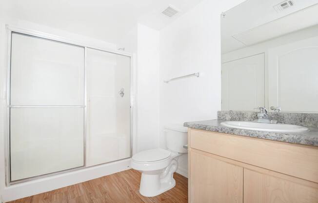 A white toilet sits in a bathroom with a marble counter and a walk-in shower.
