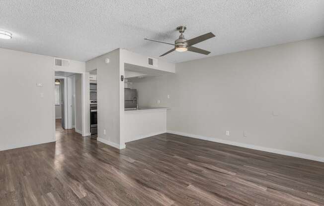 an empty living room with a ceiling fan and a kitchen