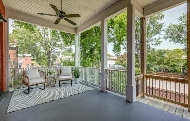 A porch with a ceiling fan and two chairs.