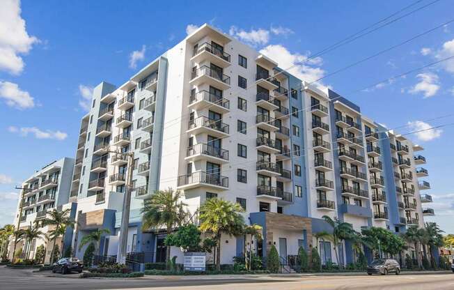 A large white and blue apartment building with balconies and palm trees in front at Alameda West Apartments in Miami, FL