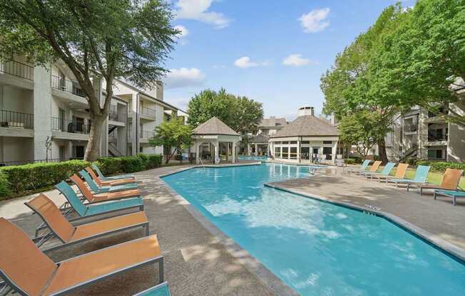A pool surrounded by lounge chairs and trees.