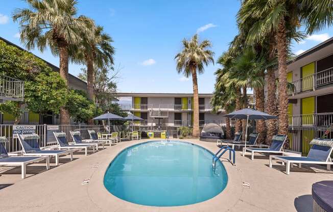 a swimming pool with chaise lounge chairs and palm trees in front of a hotel