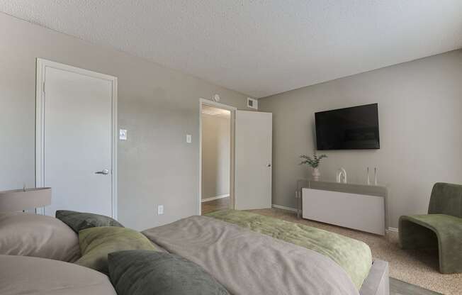 A bedroom with a bed, a chair, and a TV on the wall.