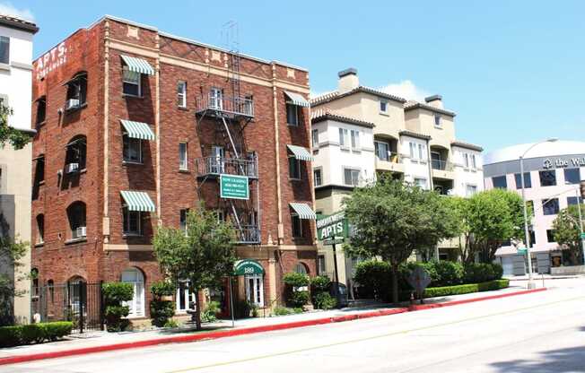 Street view of Brookmore apts in Pasadena CA. Four story brick building with striped awnings, fire escape, and "now leasing" sign.