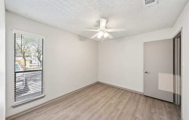 an empty living room with a window and a ceiling fan