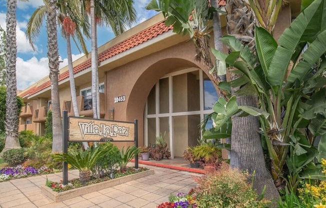 a building with a sign in front of it and palm trees at Villa La Paz Apartments, Bellflower, CA, 90706