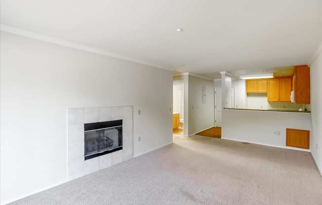 A large, empty living room with a fireplace and a kitchen in the background.