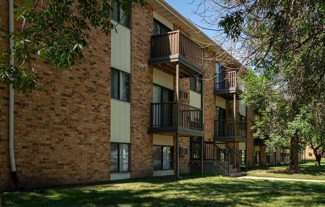 A brick building with balconies and trees in front. Bismarck, ND Garden Grove Apartments