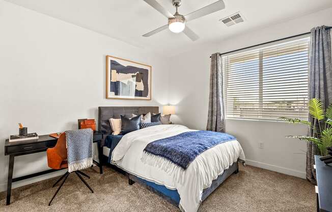 A bedroom with a bed, desk, chair, and a ceiling fan.