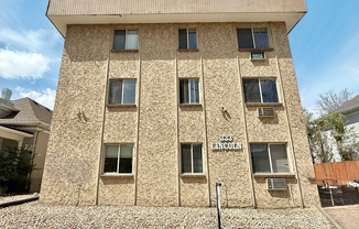 Charming three-story apartment building with textured exterior, surrounded by a neat stone landscape under a clear sky.