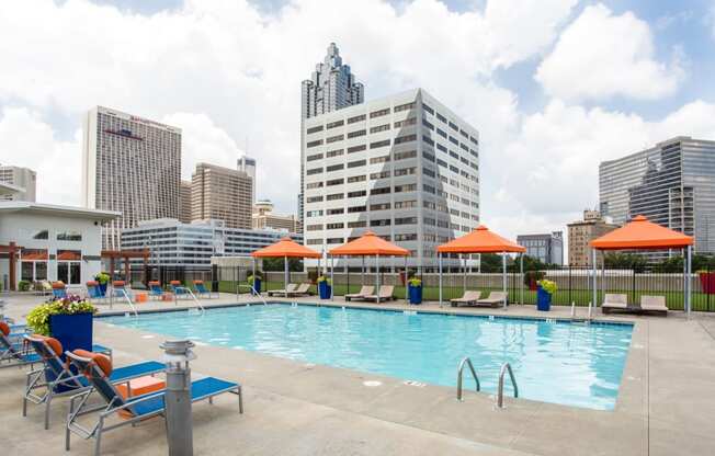 a swimming pool with chairs and umbrellas next to a city skyline