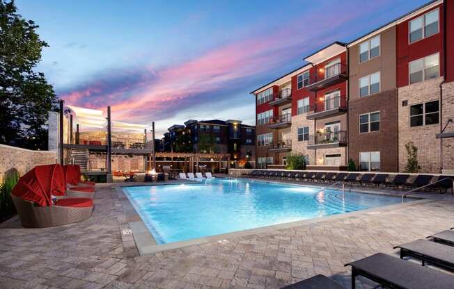 an outdoor swimming pool at dusk with an apartment building in the background