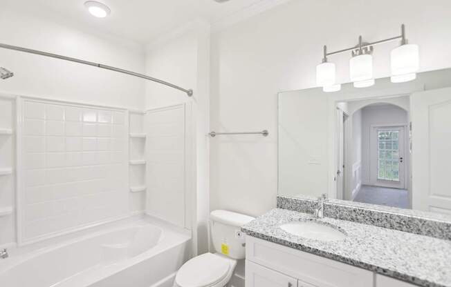 A bathroom with a tub, toilet, and granite sink.