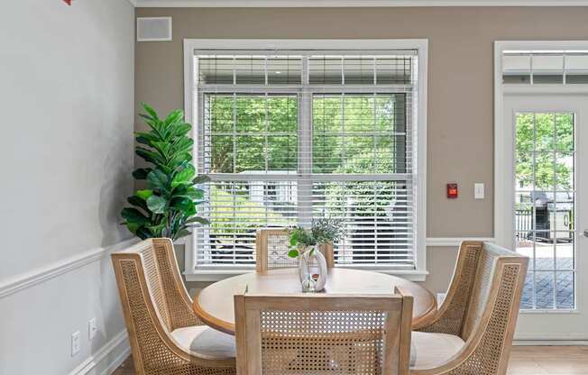 A table with chairs and a vase of flowers in front of a window.