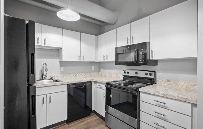 A black refrigerator is in a kitchen with white cabinets and a marble countertop.