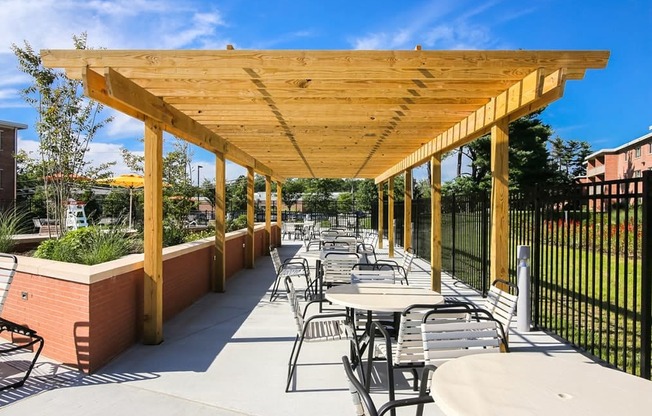 A wooden pergola with tables and chairs is set up on a patio.