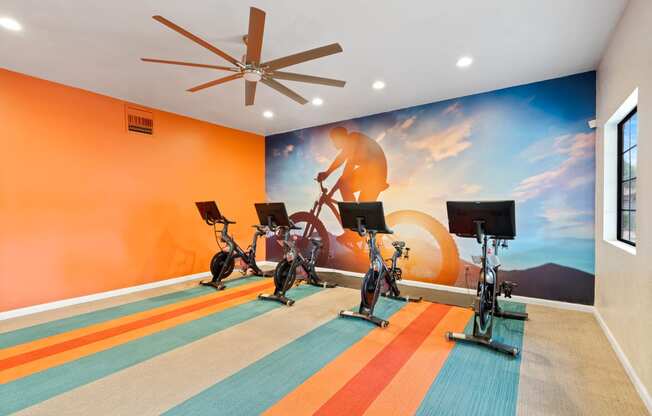 Gym with exercise bikes and a mural of a man riding a bike at Verde Apartments in Tucson, AZ.